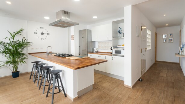 Una cocina moderna con una isla central, taburetes de bar, un reloj y electrodomésticos de acero inoxidable.