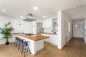A modern kitchen with a central island, bar stools, a clock, and stainless steel appliances. - Casa Punta Brava, terrace with sea views in Puerto de la Cruz (Puerto de la Cruz)