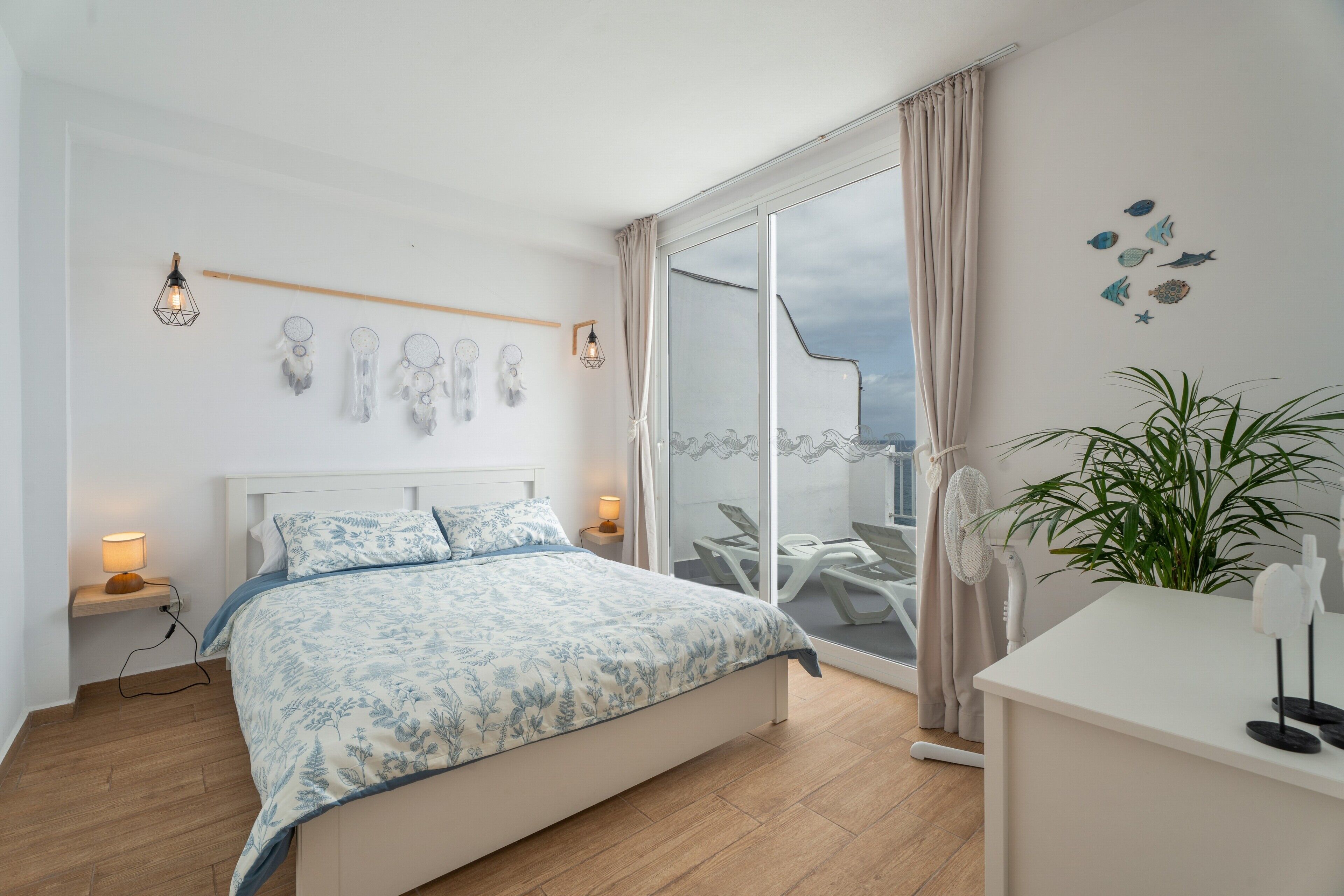 Ein Schlafzimmer mit Bett, Nachttischlampen, einem Nachttisch, einer Topfpflanze und Blick nach draußen.