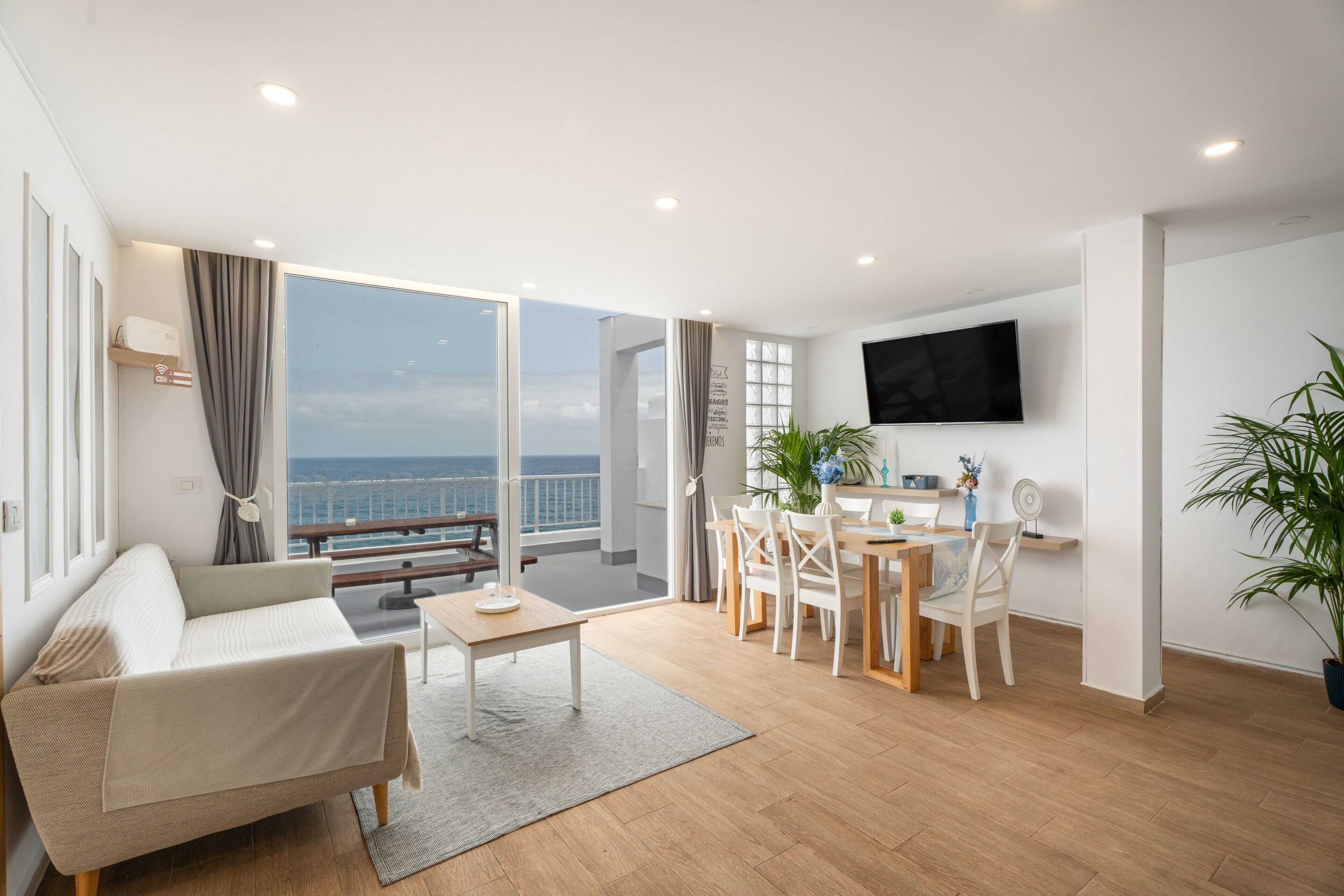 Ein modernes Wohnzimmer mit einer Couch, einem Esstisch, Stühlen, einem Fernseher und Blick aufs Meer.