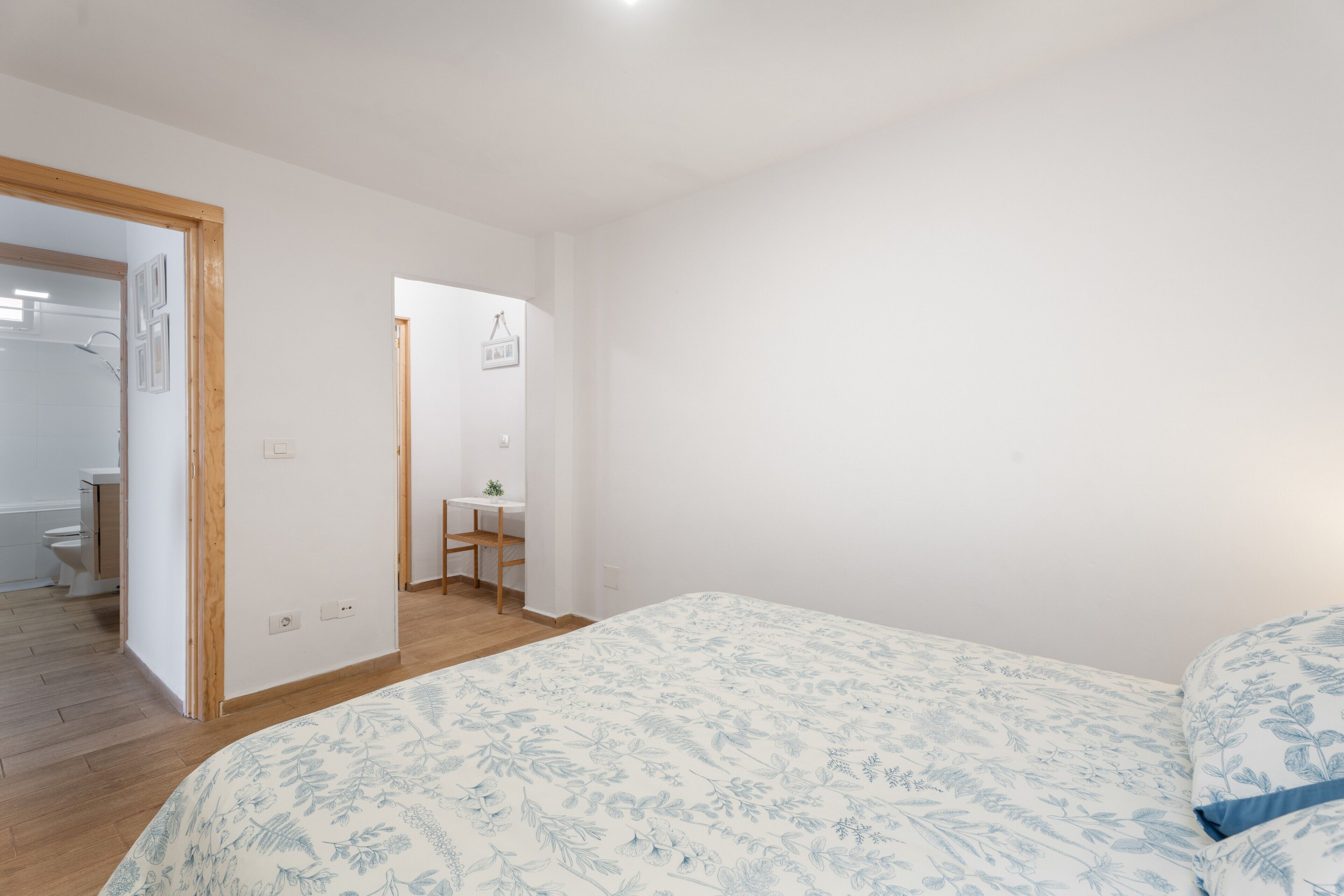 Un dormitorio con cama, piso de madera y baño visible a través de una puerta abierta.
