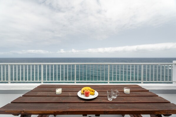 A wooden table with a plate of food, a glass of milk, and a banana on a balcony overlooking the sea.