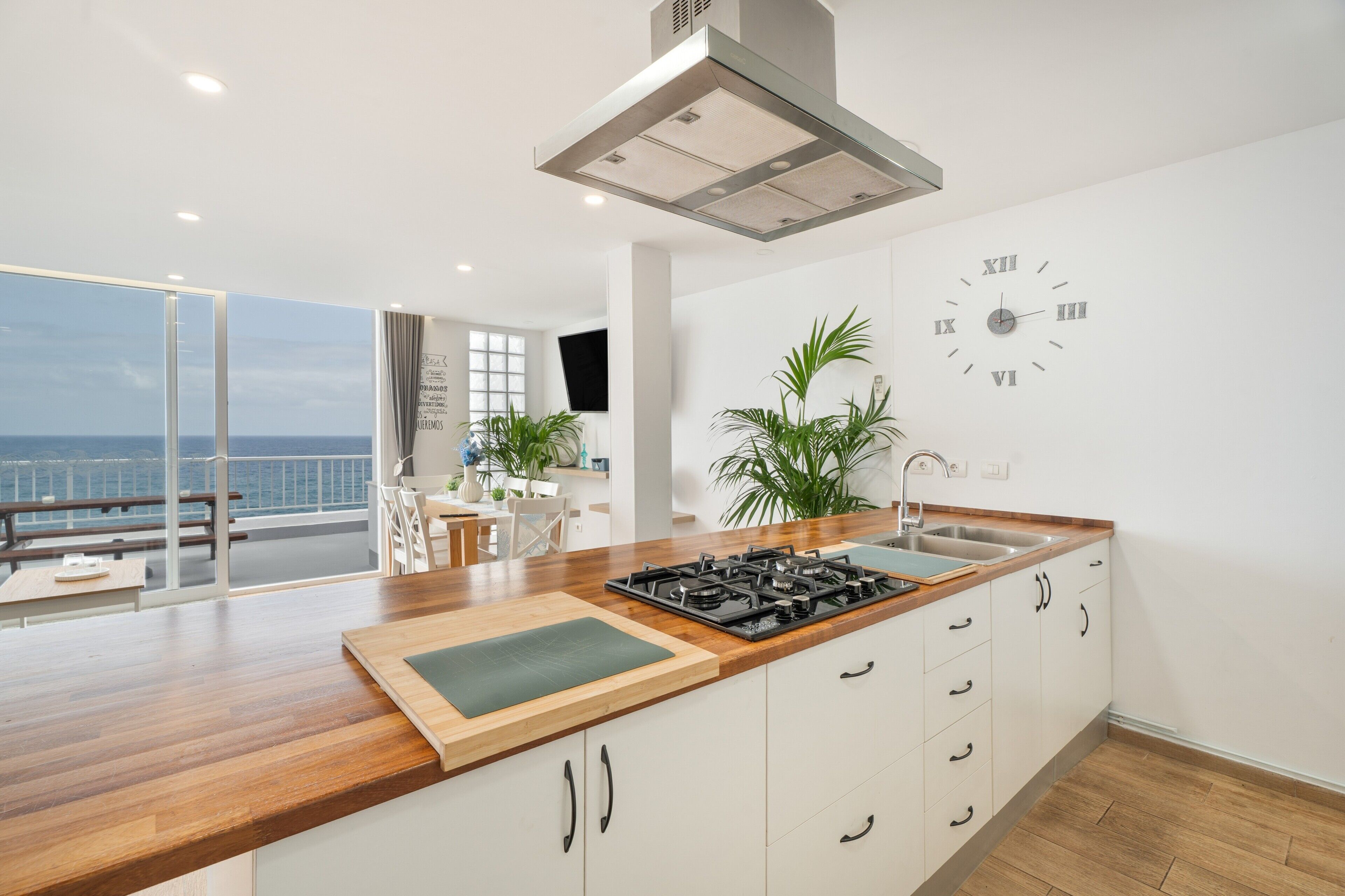 Een moderne keuken met een groot eiland, een ingebouwde kookplaat en uitzicht op zee door een schuifdeur.