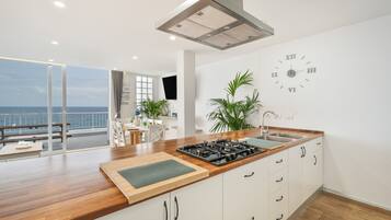 Een moderne keuken met een groot eiland, een ingebouwde kookplaat en uitzicht op zee door een schuifdeur.