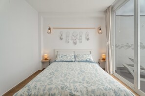 Une chambre avec un grand lit, deux tables de chevet avec des lampes, un attrape-rêves accroché au mur et une vue sur un balcon.