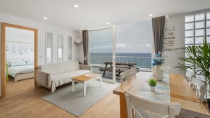 Una sala moderna con un sofá, una mesa de centro y un comedor con sillas y una mesa. Hay un ventanal con vistas al mar.