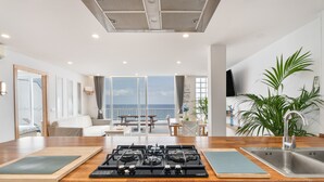 Una cocina moderna con estufa a gas, un lavamanos y vistas al mar a través de amplios ventanales.