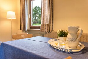 Une table recouverte d’une nappe bleue, avec une carafe, un verre et une petite plante en pot.