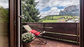 Un balcone con una sedia e una pianta in vaso, affacciato su un paesaggio montuoso e un villaggio.