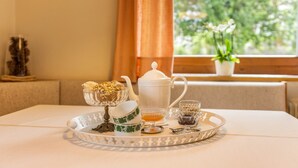 Uma mesa com bandeja contendo um bule, xícaras e tigelas, em frente a uma janela com vista para o verde.