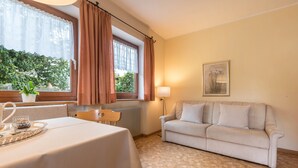 Um quarto com uma mesa de jantar, um sofá, um radiador, uma janela com cortinas e um quadro na parede.