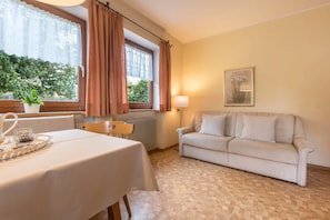 A room with a dining table, a sofa, a radiator, a window with curtains, and a framed picture on the wall.