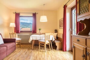 Une pièce comprenant une table à manger, des chaises, un canapé, un radiateur et une fenêtre avec des rideaux.