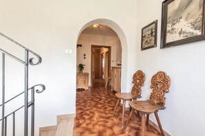 A hallway with a checkered floor, an arched doorway, and two ornate wooden chairs.