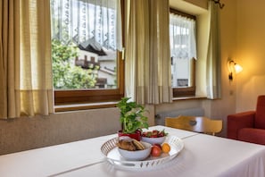 A breakfast tray with croissant, strawberries, and peaches on a table with a view of a building through a window.