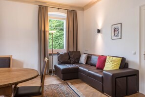 A living room with a brown leather sofa, a wooden dining table, and a patterned rug. - Villa Martiner Apartments Francesco with Mountain View, Balcony & Wi-Fi (Ortisei)