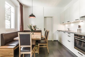 A modern kitchen with a dining area, featuring a wooden table, chairs, a pendant light, and a built-in oven. - Villa Martiner Apartments Francesco with Mountain View, Balcony & Wi-Fi (Ortisei)