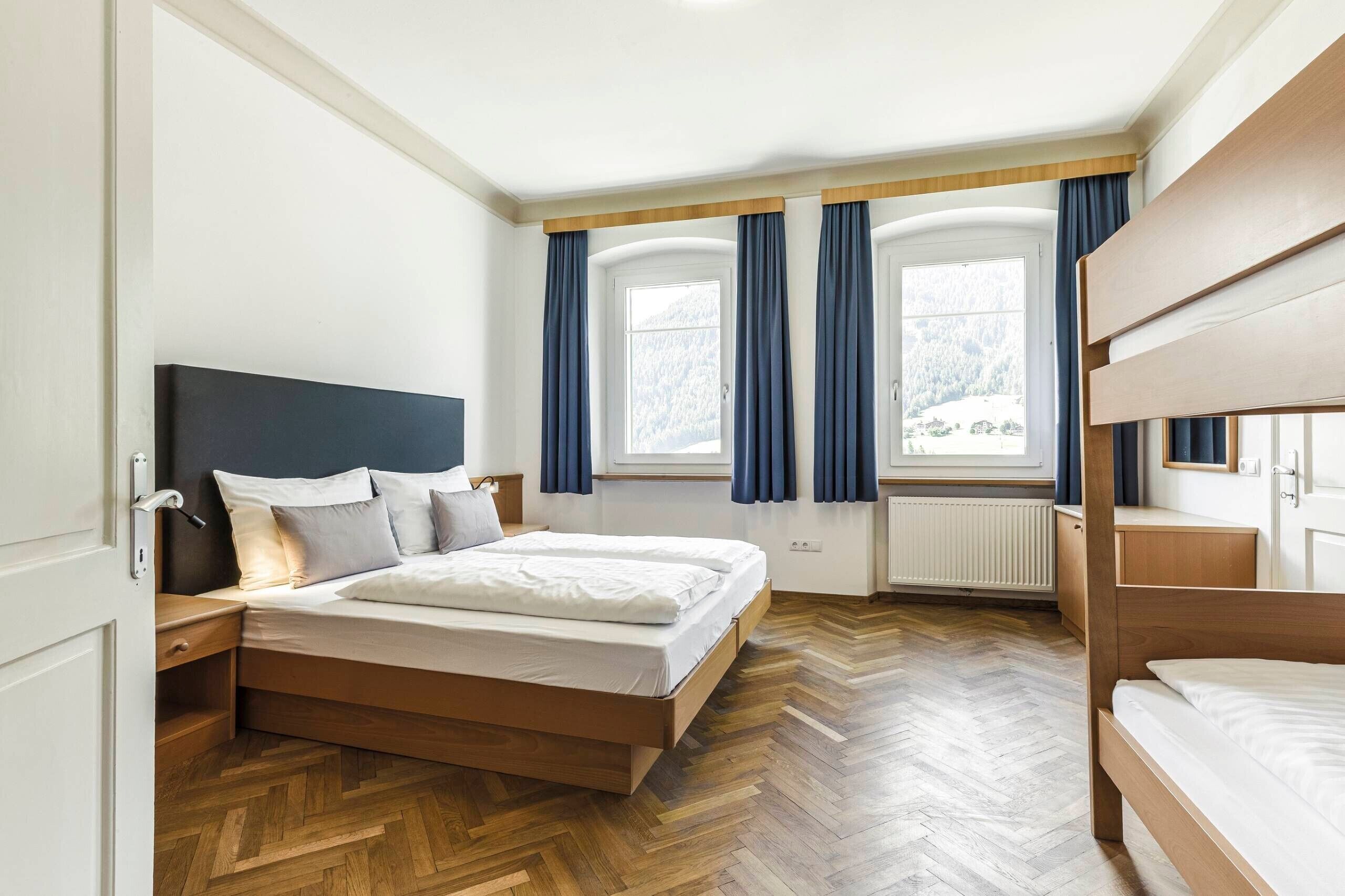 Ein Schlafzimmer mit Bett, Nachttisch, einem Fenster mit Vorhängen und einer Heizung.