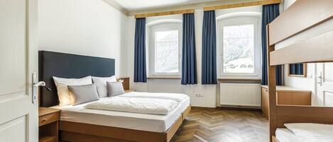 Ein Schlafzimmer mit Bett, Nachttisch, einem Fenster mit Vorhängen und einer Heizung.