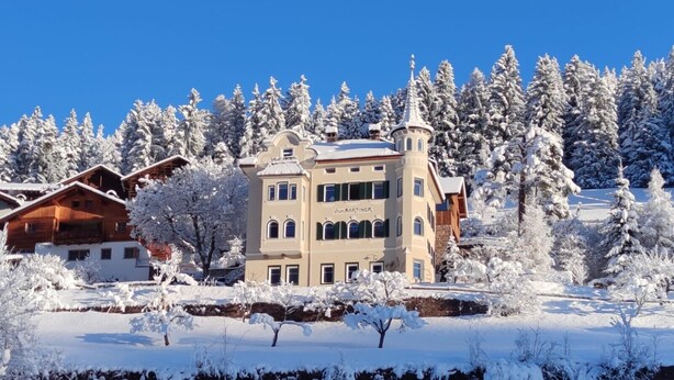 Ein mehrstöckiges Gebäude mit einem Turm, umgeben von schneebedeckten Bäumen und blauem Himmel.