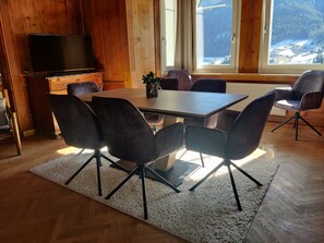 A wooden interior with a dining table, chairs, a television, and a window with a snowy view. - Villa Martiner Apartments Emilia with Mountain View, Terrace & Wi-Fi (Ortisei)