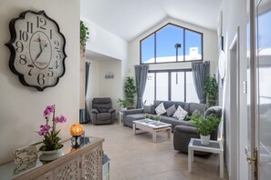 Un salon spacieux, agrémenté d’une grande horloge, d’un ensemble de canapés, d’une table basse et offrant une vue dégagée sur l’extérieur grâce à une grande fenêtre.