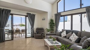 Ein geräumiger Wohnbereich mit Sofa, Sessel und Esstisch, großen Fenstern und einer Glastür zum Außenbereich.