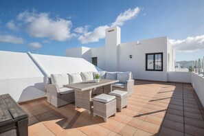 Une terrasse sur le toit avec un mur blanc, une table et des meubles en osier.