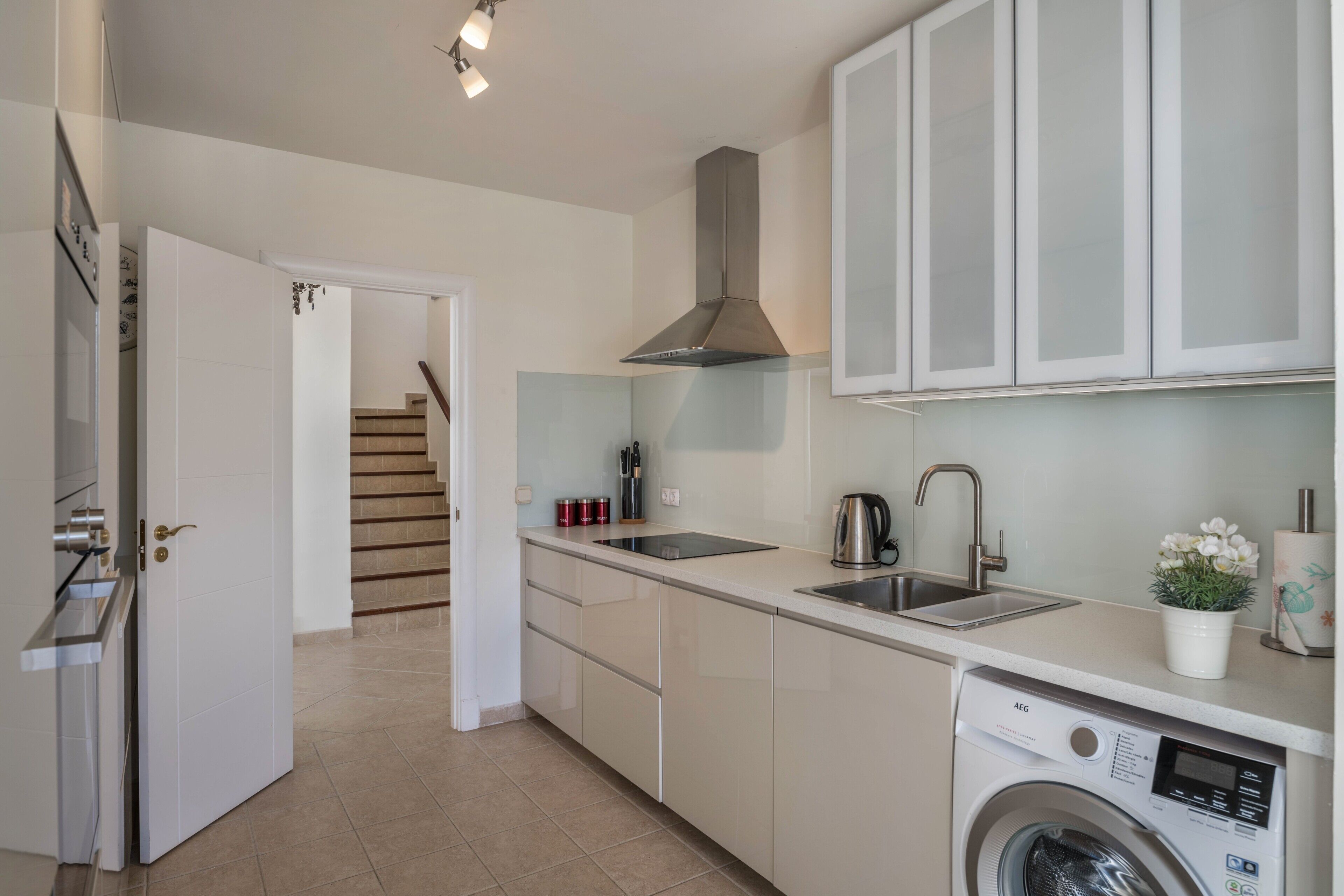 A modern kitchen with a built-in washing machine, a stainless steel sink, and a staircase leading to another room.