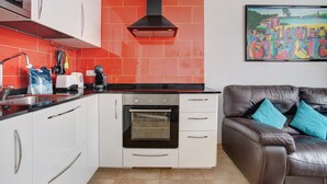 Una cocina con armarios blancos, una campana extractora negra y un salpicadero rojo.