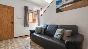 Quarto com sofá de couro escuro, ladrilhos estampados, porta de madeira, janela com cortinas e um quadro na parede.