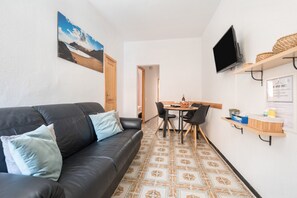 Olohuoneessa on musta nahkasohva, ruokapöytä tuoleineen, seinälle asennettu televisio ja kuviollinen lattia.