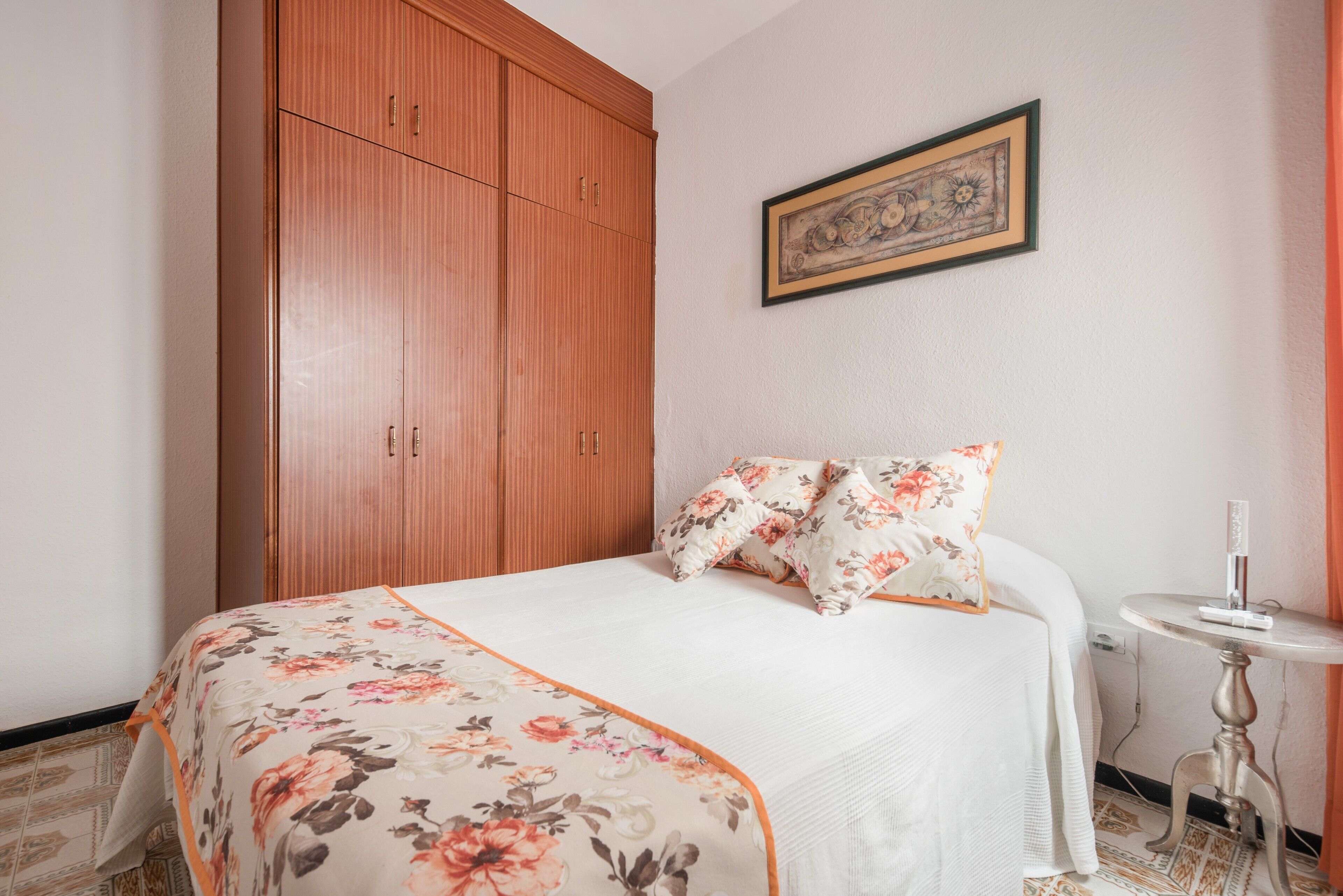Un dormitorio con una cama, un armario de madera, una mesita pequeña y un cuadro en la pared.