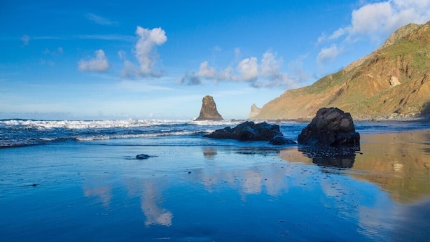 Una playa con formaciones rocosas y olas tranquilas.