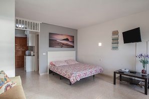 Un dormitorio con una cama, televisión, escritorio y un cuadro en la pared.