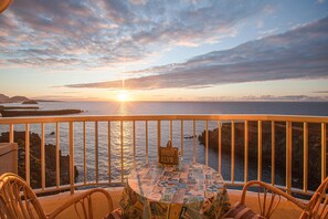 A balcony with a table and chairs, overlooking a sunset over the sea.