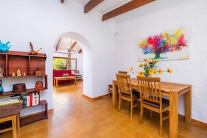 A dining area with a wooden table and chairs, a bookshelf, and a colorful abstract painting on the wall.