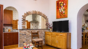 Una cocina con arco de piedra, armarios de madera, un televisor y una mesa de comedor con un jarrón de flores.