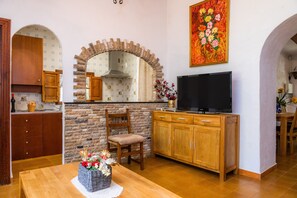 Una cocina con arco de piedra, armarios de madera, un televisor y una mesa de comedor con un jarrón de flores.