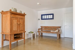 A room with a wooden cabinet, a bench, a small table with a plant, and a window with blinds.