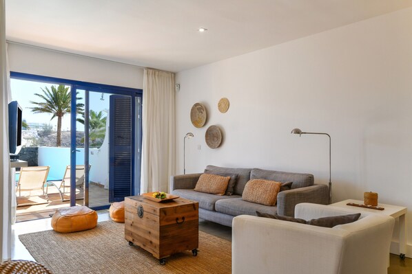 A living room with a sofa, ottoman, wooden chest, and a view of the outdoors.