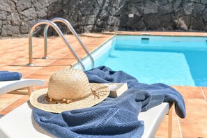 A poolside area with a lounge chair, a hat, and a book.