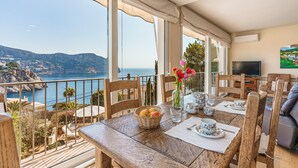 Un balcon avec vue sur la mer, une table à manger avec des chaises, un téléviseur et un tableau accroché au mur.