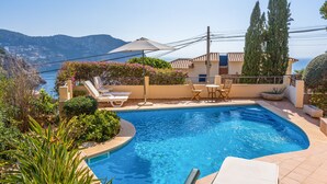 Une piscine privée avec des chaises longues, une table et une vue sur la mer et les montagnes.