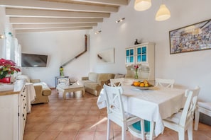 A spacious living area with a dining table, white furniture, a TV, and a cabinet with glass doors. - Villa “Ca Ses Nines” with Mountain View, Pool, Wi-Fi, A/C, Terrace & Garden (Puerto de Andratx)