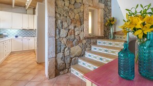 Una cocina con armarios blancos, una pared de piedra y piso de baldosas.