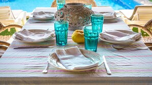 Una mesa de comedor dispuesta para cuatro, con un jarrón decorativo, copas de vidrio azules y un limón sobre el mantel.