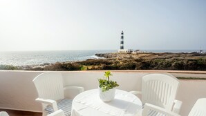 Una terraza con sillas y una mesa blancas, con vistas a la costa y un faro.