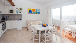 Una cocina moderna con armarios blancos, microondas y un comedor con sillas y mesa blancos.