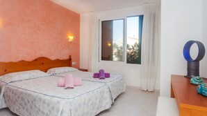 A bedroom with two beds, a wooden headboard, a window with curtains, a desk with a chair, and a decorative item on the desk. - Apartment Cala en Forcat 36 with Balcony & Shared Pool (Cala en Blanes)